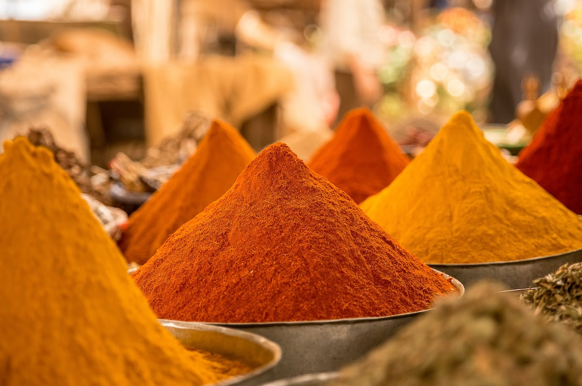 Cone-shaped mounds of turmeric and colorful ground spices displayed in bowls at a market.