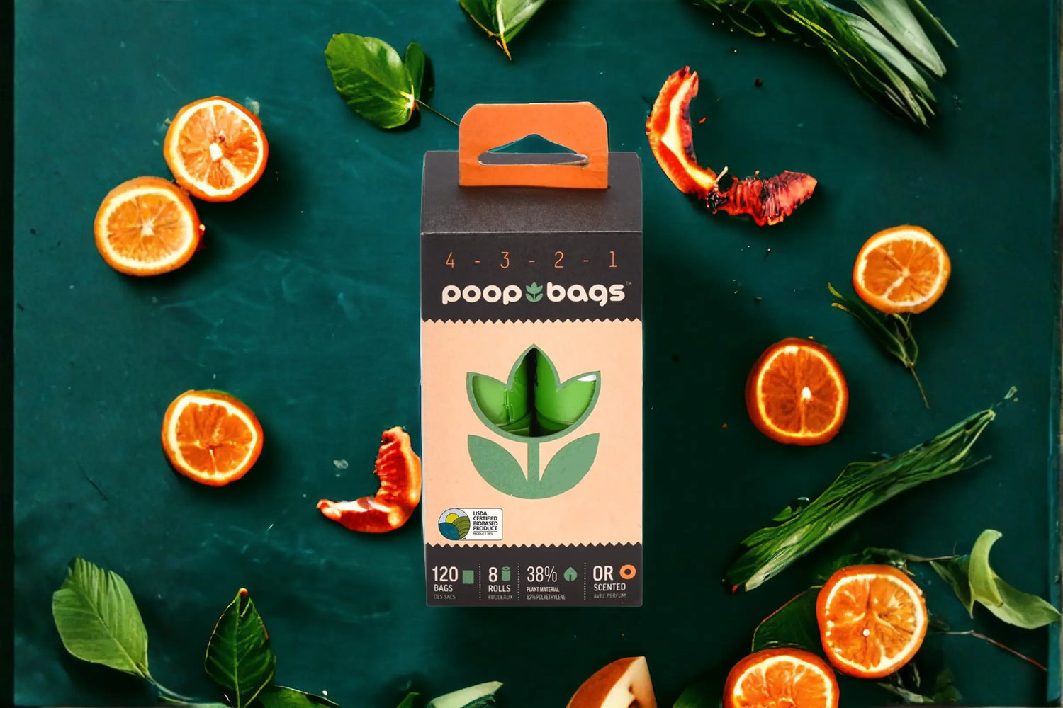Box of The Original Poop Bags sustainable pet waste bags with orange-scented rolls, surrounded by sliced citrus fruits and fresh green leaves on a teal surface.