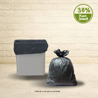 Black plant-based trash can liner inside a white bin with a tied bag beside it showing 38 percent plant-based material badge.