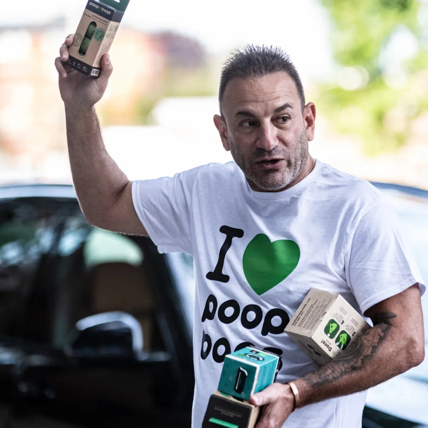 Man in 'I love poop bags' t-shirt holding eco-friendly dog waste bag dispensers and products